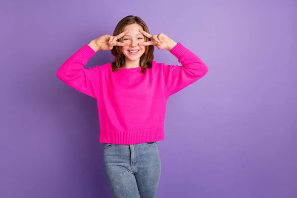 Zdjęcie wesoły cute cool girl zrobić palce v-signs nosić różowy sweter dżinsy izolowane na fioletowym tle koloru — Zdjęcie stockowe