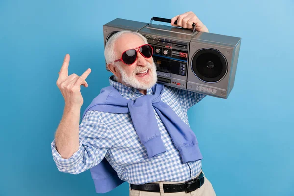 Фотографія оптимістичного старого сірого чоловіка, що показує рок-знак, тримає бум-бокс одягати окуляри синя сорочка ізольована на кольоровому фоні — стокове фото