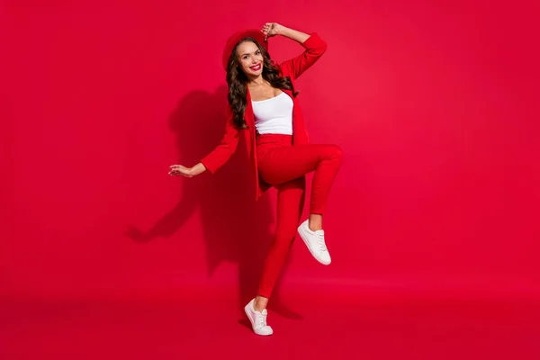 フルボディ写真の感銘を受けたブルネット女性ダンスウェアキャップスーツスニーカー隔離された赤の色の背景 — ストック写真