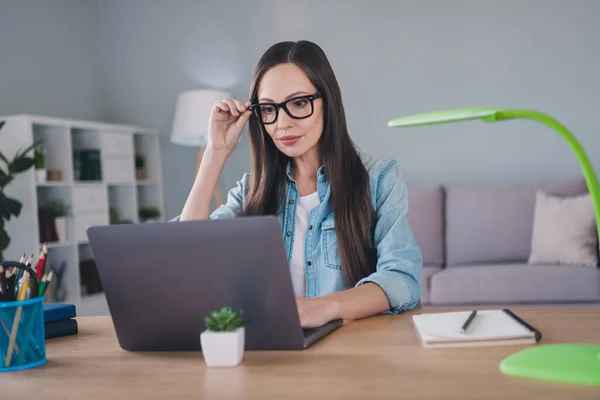 Foto van gerichte serieuze volwassen vrouw kijken laptop zitten bureau werkplaats dragen bril binnen huis — Stockfoto