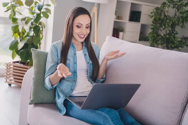 Retrato de mujer atractiva de pelo largo alegre sentado en diván usando el ordenador portátil llamando a un amigo de la web en casa en interiores —  Fotos de Stock