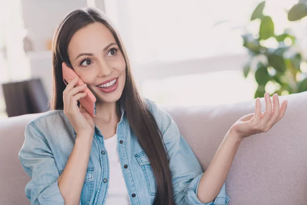 Retrato de mulher de cabelos compridos alegre atraente sentado no divã chamando amigo roaming celular em casa dentro de casa — Fotografia de Stock