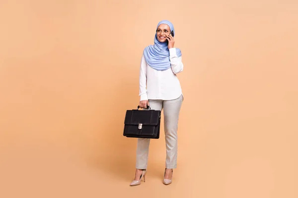 Full body photo of millennial arabic modern lady with bag talk telephone wear headscarf shirt eyewear pants stilettos isolated on beige background — Stock Photo, Image