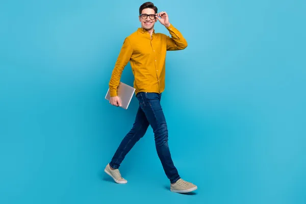 Foto van zakenman man houden laptop lopen dragen gele shirt jeans sneakers geïsoleerde blauwe kleur achtergrond — Stockfoto