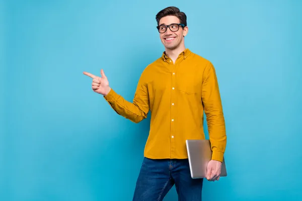 Foto van koele brunet hr man hold laptop geven lege ruimte dragen geel shirt brillen geïsoleerd op blauwe kleur achtergrond — Stockfoto