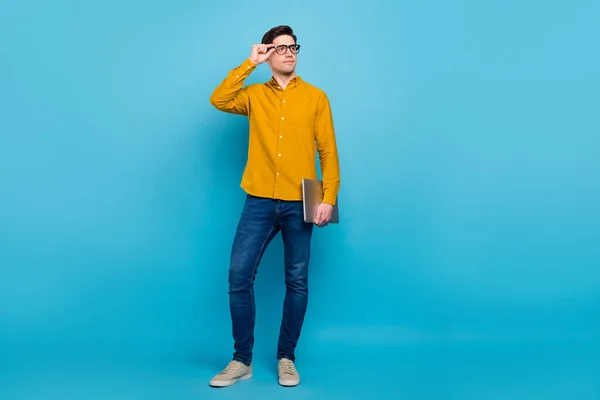Fotografie zvědavý smýšlející chlap držet ks vzhled prázdný prostor oblečení žlutá košile džíny boty izolované modré barvy pozadí — Stock fotografie