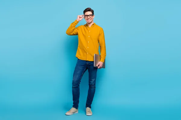 Full längd foto av smart brunett ceo man hålla bärbar dator bära gul skjorta glasögon jeans sneakers isolerade på blå färg bakgrund — Stockfoto
