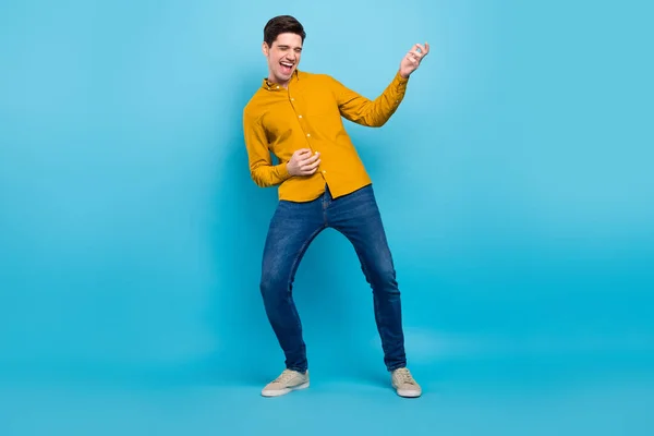 Foto de cara engraçado jogar guitarra imaginária usar camisa amarela calça calçado isolado azul cor de fundo — Fotografia de Stock