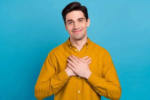 Zdjęcie wesoły wdzięczny facet ręce klatka piersiowa serce forma nosić żółty koszula odizolowany niebieski kolor tło — Zdjęcie stockowe