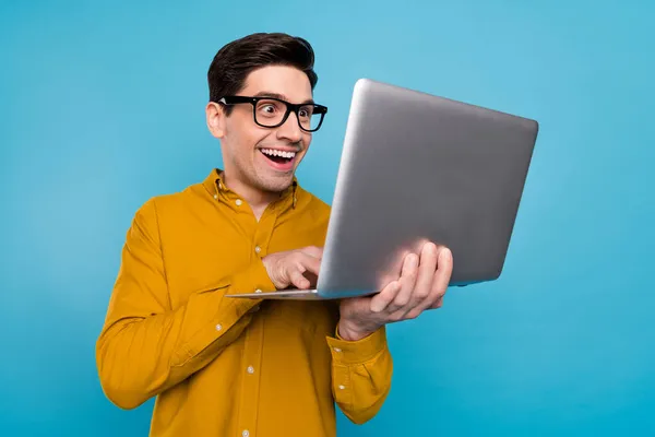 Foto de surpreendido cara surpreso segurar netbook look screen desgaste óculos amarelo camisa isolado azul cor fundo — Fotografia de Stock