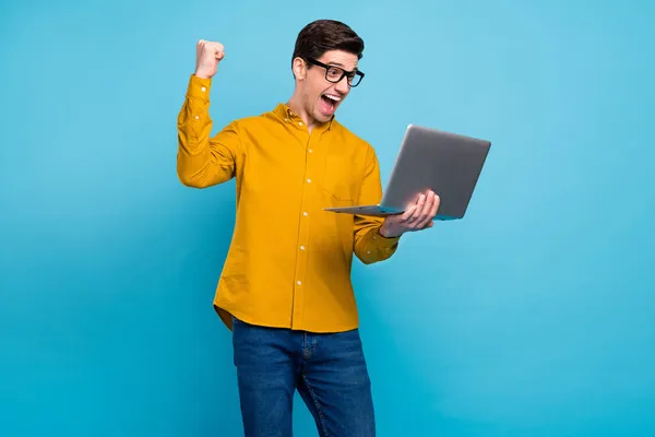 Фото дивовижного брюнетки чоловік тримає ноутбук у жовтій сорочці окуляри ізольовані на синьому кольорі — стокове фото