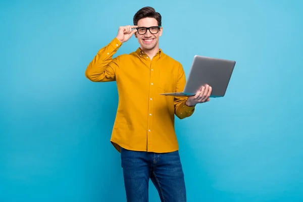 Photo of cheerful guy hold netbook shiny smile wear eyeglasses yellow shirt isolated blue color background — Stock Photo, Image