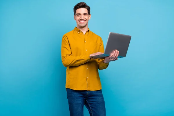 Zdjęcie pozytywnego wesoły facet trzymać laptop promieni uśmiech nosić żółtą koszulę odizolowany niebieski kolor tła — Zdjęcie stockowe