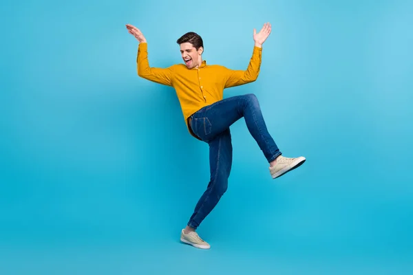 Foto de cara despreocupado funky dança levantar as mãos usar camisa amarela jeans sapatos isolado azul cor de fundo — Fotografia de Stock