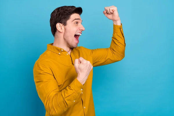 Perfil foto de alegre campeão cara comemorar vitória espaço vazio desgaste amarelo camisa isolado azul cor fundo — Fotografia de Stock