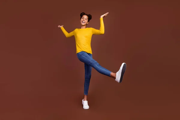 Foto de longitud completa de niña pequeña danza desgaste suéter jeans calzado aislado sobre fondo de color marrón —  Fotos de Stock