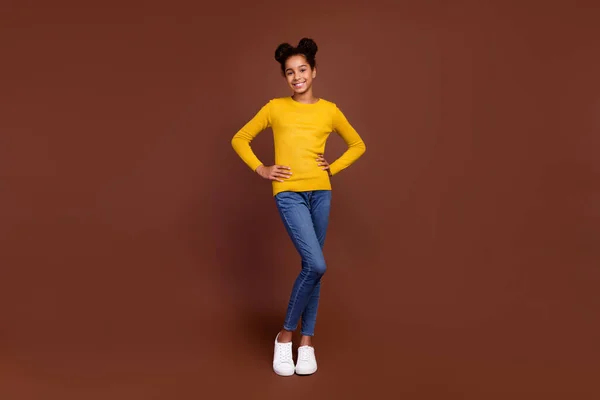 Foto de longitud completa de dulce niña pequeña ropa fresca jersey jeans calzado aislado sobre fondo de color marrón —  Fotos de Stock