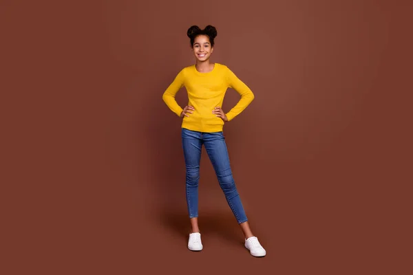 Teljes méretű fotó aranyos tizenéves lány stand viselni jumper farmer cipő elszigetelt barna színű háttér — Stock Fotó