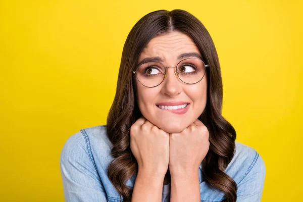 Photo of pretty charming young woman dressed denim shirt glasses biting lip arms chin looking empty space isolated yellow color background — Stock Photo, Image