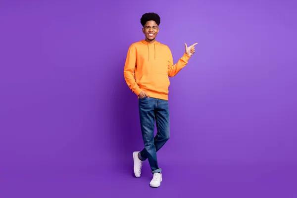 Foto de tamaño completo de la piel joven oscura hombre feliz dedo dedo vacío espacio publicitar pantalones vaqueros aislados sobre fondo de color violeta — Foto de Stock
