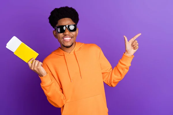 Foto di marrone capelli afro americano uomo indossare felpa con cappuccio punto di occhiali da sole spazio vuoto tenere i biglietti isolati su sfondo di colore viola — Foto Stock