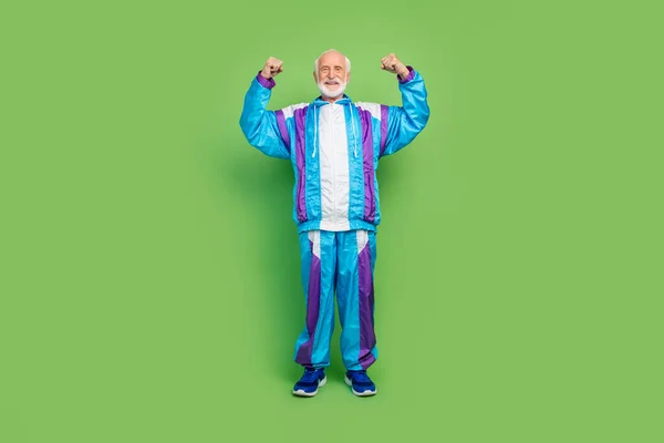 Fotografie funky cool senior muž nosit sportovní oblek ukazující biceps s úsměvem izolované zelené barvy pozadí — Stock fotografie