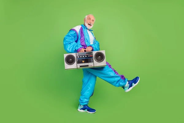 Komik, olgun, mavi takım elbiseli, gülümseyen, yürüyen, müzik kutusunu dinleyen yeşil renkli bir adamın fotoğrafı. — Stok fotoğraf