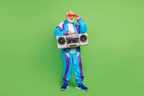 Foto de engraçado homem muito sênior usar terno esportivo óculos escuros ouvir boombox sorrindo isolado cor verde fundo — Fotografia de Stock