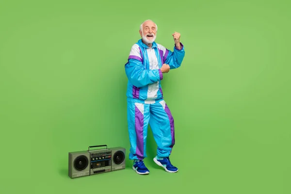 Komik, olgun bir adamın mavi spor giyinmiş, gülümseyen müzik kutusu dinleyen yeşil renkli arka plan dansçısının fotoğrafı. — Stok fotoğraf