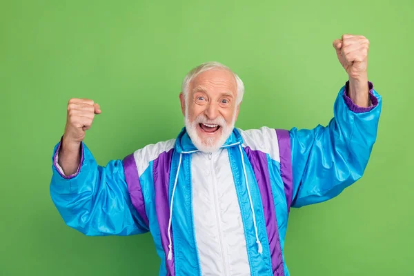 Foto de hombre mayor funky suerte usar traje deportivo puños ascendentes sonriendo aislado fondo de color verde — Foto de Stock