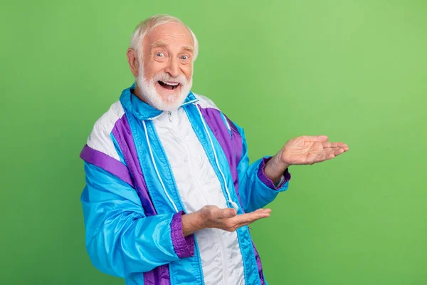 Zdjęcie pod wrażeniem dość starszy mężczyzna nosić sportowy garnitur uśmiechnięty trzymając ramiona puste miejsce odizolowane zielony kolor tło — Zdjęcie stockowe