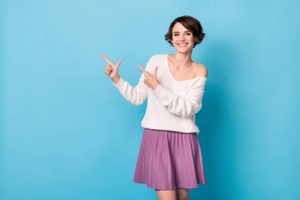 Retrato fotográfico de una chica positiva apuntando con dos dedos al espacio en blanco aislado sobre fondo de color azul pastel — Foto de Stock