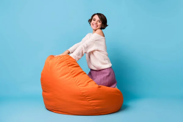 Portrait photo vue complète du corps de l'adorable fille assise sur les genoux dans une chaise de haricot orange isolée sur fond bleu pastel — Photo