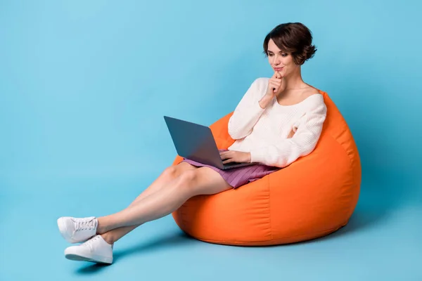 Foto potret seluruh tubuh melihat gadis berpikir dengan laptop duduk di kursi beanbag oranye terisolasi di latar belakang berwarna biru pastel — Stok Foto