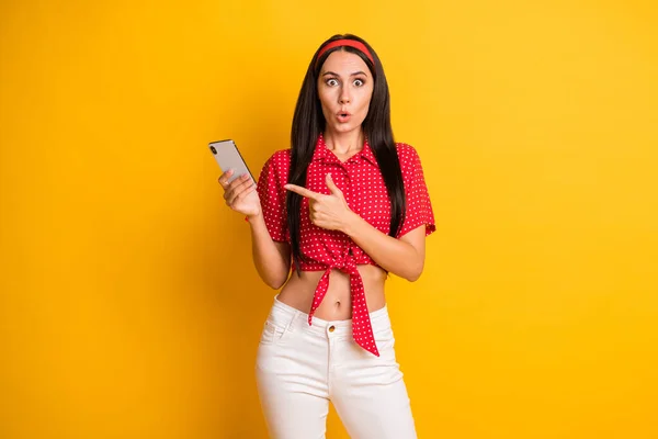 Fénykép aranyos lenyűgözött fiatal hölgy viselni piros ing mutató modern szerkentyű izolált sárga színű háttér — Stock Fotó