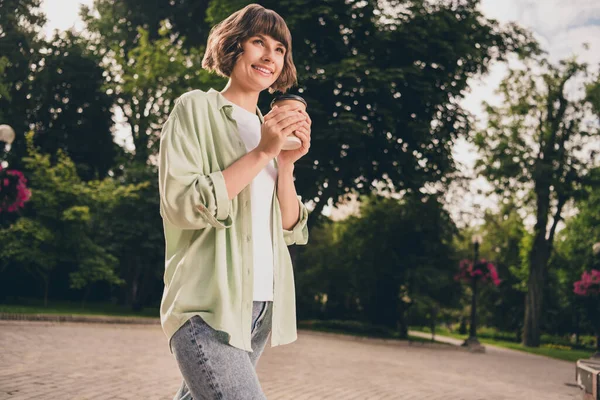 Foto von charmanten hübschen jungen Dame gekleidet grünes Hemd zu Fuß trinken Getränk Lächeln im Freien Stadtpark — Stockfoto