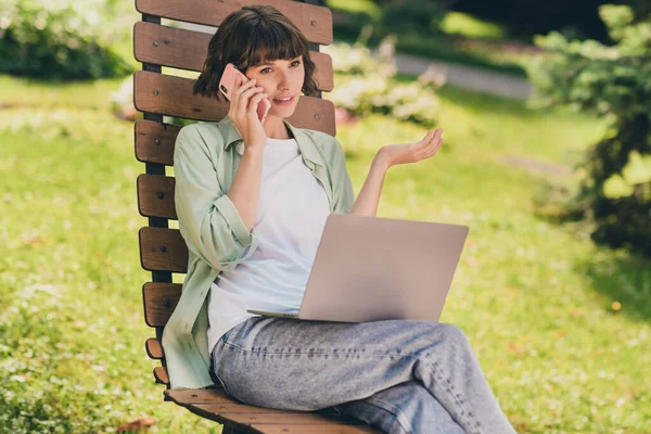 Portret zdjęcie uśmiechnięta młoda dziewczyna siedzi na ławce pracując na laptopie rozmawiając przez telefon komórkowy w zielonym parku — Zdjęcie stockowe