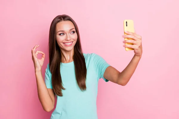 照片上年轻快乐的微笑积极乐观的心情女人在手机上自拍，显示出在粉色背景下孤立的好迹象 — 图库照片