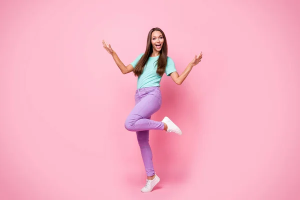 Foto ukuran penuh dari wanita muda yang tersenyum gembira tarian wanita cantik mengenakan t-shirt teal dan celana ungu terisolasi di latar belakang warna merah muda — Stok Foto