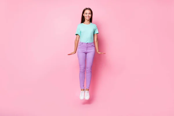 年轻迷人的笑容满面的女人穿着紫色裤子，紧挨粉色背景的T恤的全长照片 — 图库照片