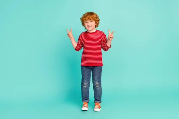 全身写真のファンキーな小さな男の子ショーvサイン着用シャツジーンズスニーカー隔離された青の背景 — ストック写真