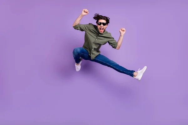 Foto in voller Größe von verrückt cool glücklich junger Mann springen Sieger tragen Sonnenbrille isoliert auf violettem Hintergrund — Stockfoto