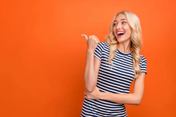 Foto portret blonde vrouw dragen gestreept t-shirt wijzen copyspace met duim geïsoleerde levendige oranje kleur achtergrond — Stockfoto