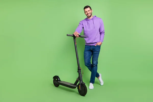 Foto de longitud completa de joven alegre hombre feliz sonrisa positiva caminar scooter eléctrico aislado sobre fondo de color verde —  Fotos de Stock