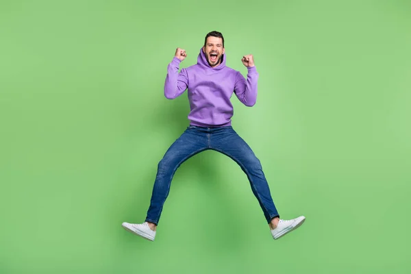 Full storlek foto av hurra tusenårig brunett kille hoppa slitage hoodie jeans sneakers isolerad på grön bakgrund — Stockfoto