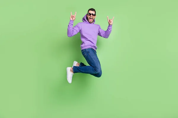 Foto de perfil de cuerpo completo de chico morena joven funky salto espectáculo rock desgaste gafas sudadera con capucha jeans zapatillas aisladas sobre fondo verde —  Fotos de Stock