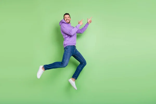 Full size profile photo of funny young brunet guy jump point wear hoodie jeans sneakers isolated on green background — Stock Photo, Image