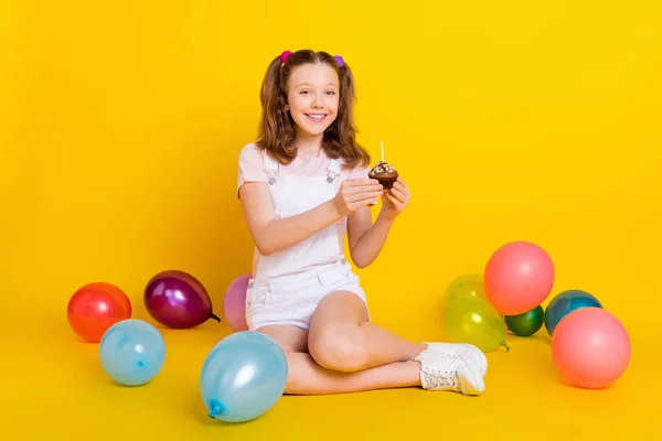 Ganzkörpergröße Foto Schulmädchen auf Party lächelnd halten Cupcake mit Kerzen isoliert helle gelbe Farbe Hintergrund — Stockfoto