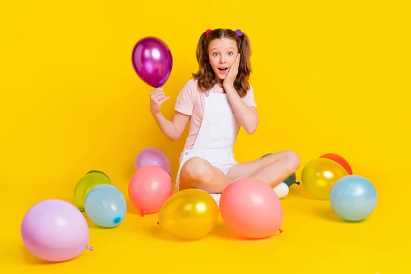 Retrato de chica alegre bastante sorprendido sosteniendo bolas de aire sentado en el suelo aislado sobre fondo de color amarillo brillante — Foto de Stock