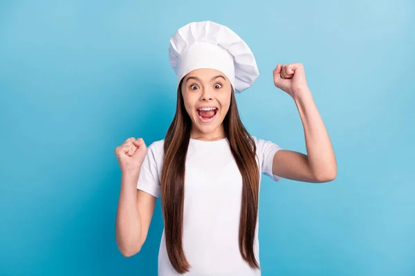 Foto di stupito scioccato felice bambina alzare i pugni vincitore culinaria indossare cappello isolato su sfondo di colore blu — Foto Stock